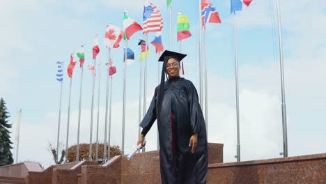 young african american woman rejoices with a diploma of higher education in hand on the street against the background of flags of different countries in europe and the world. master of pharmacy