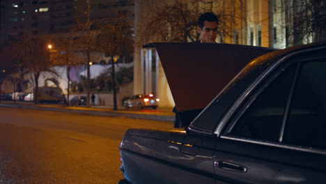 Confident tourist opening car trunk at night. Businessman getting travel luggage