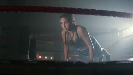 joven deportista caucásica con coletas trenzadas haciendo flexiones en el ring de boxeo