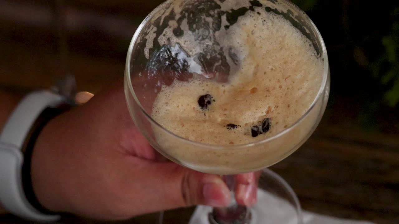A hand holds an espresso martini with flies inside, captured in a Phuket bar setting