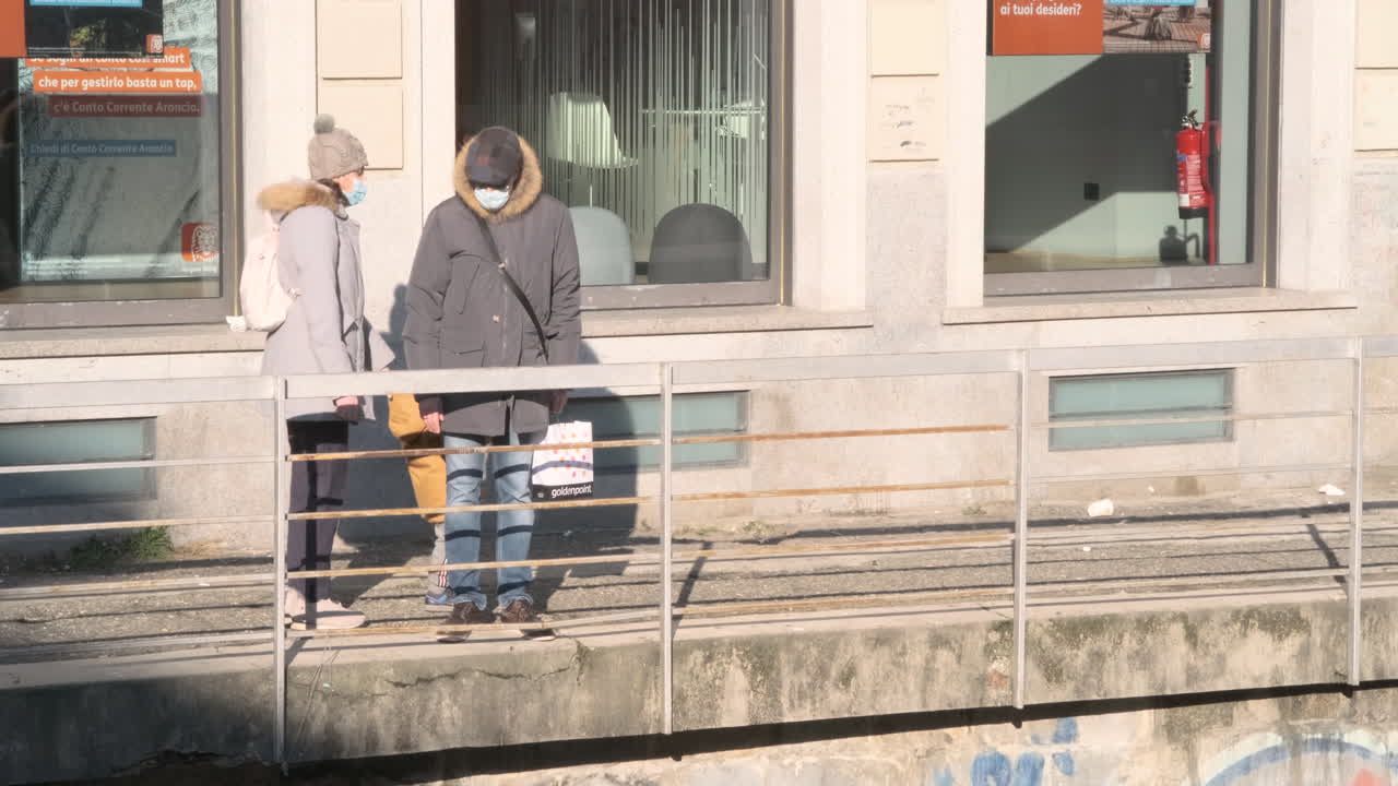 A Family Wearing Face Mask Stroll Near Railing In the City Center On A Sunny Day Of Winter In Monza, Northern Italy - wide, static shot
