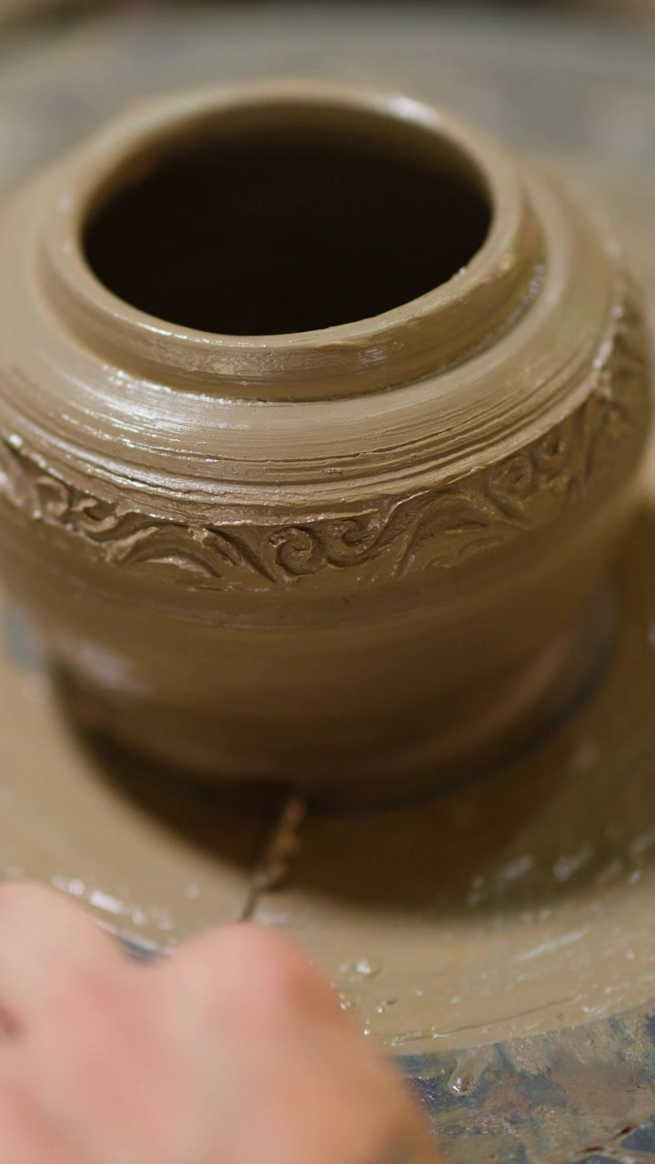 Primo piano di mani che modellano un vaso di argilla bagnata con motivi intricati a Nonthaburi, Thailandia.