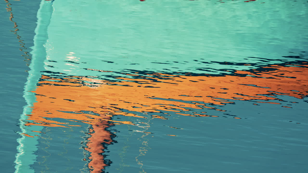 Abstract reflection of colorful boat hulls rippling across the surface of the water, creating a painterly effect