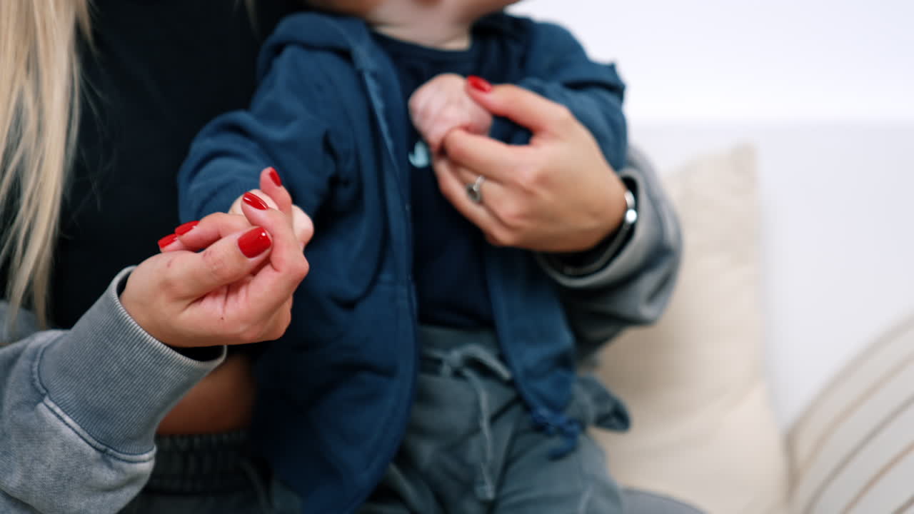 Unrecognized blonde woman holding a baby in hands. Mother is waving little son's hand. Close up.