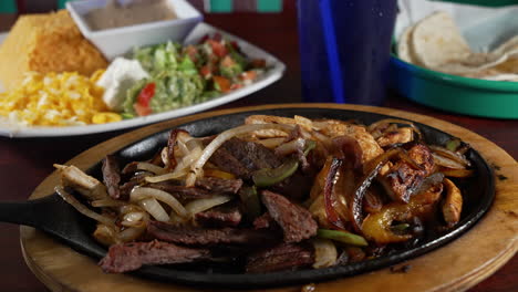 Una-Sartén-Chisporroteante-De-Combinación-De-Fajitas-De-Res-Y-Pollo-Con-Tortillas-Arroz-Frijoles-Refritos-Queso-Guacamole,-Deslizador-4k