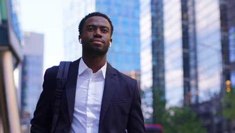 young businessman wearing wireless earbuds streaming music or podcast from mobile phone walking to work in offices in the financial district of the city of london uk 2