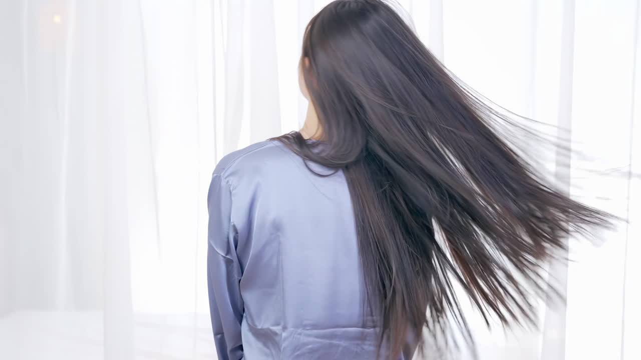 มุมมองด้านหลังของหญิงสาวกำลังสะบัดศีรษะพร้อมผมยาวสลวยที่พลิ้วไหว อวดผมสีดำสวยงามที่พลิ้วไหวอย่างมีสไตล์หลังจากไปร้านเสริมสวย