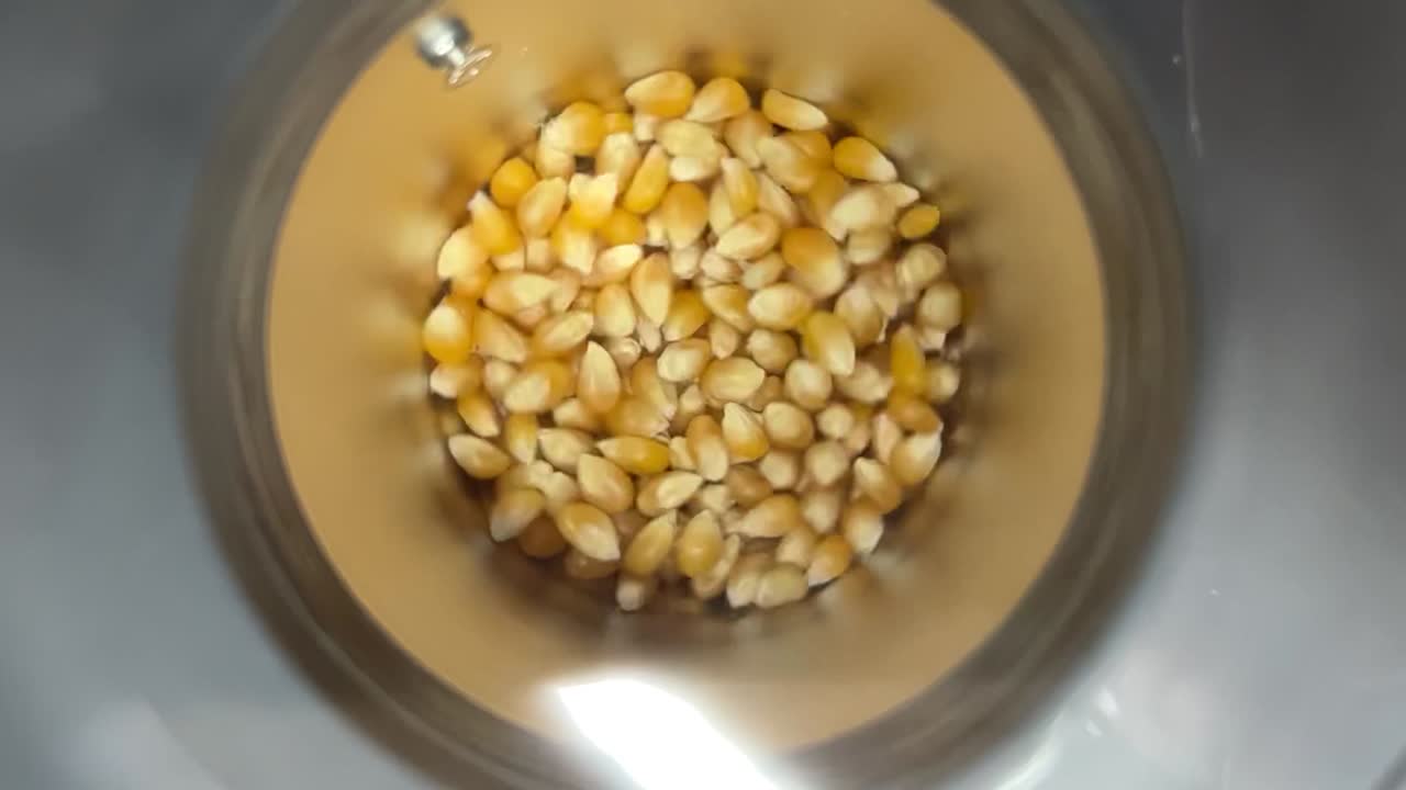 Hot air popcorn machine rotating fresh corn with hot air turbine. Converting corn into popcorn with dry hot air. Corn popping in a hot air popper. Corn popping and flying from machine to the bowl