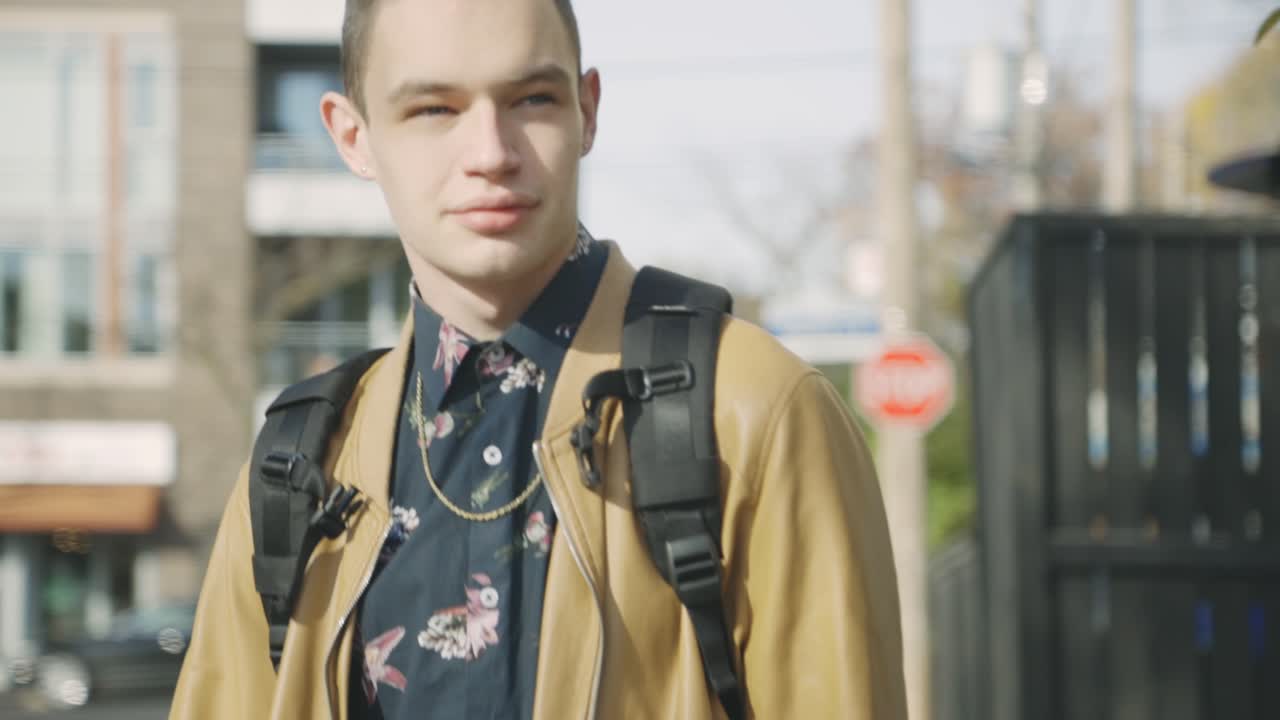 갈색 코트와 배낭을 메고 도시 거리를 걷고 있는 평범한 청년 - 슬로우 모션