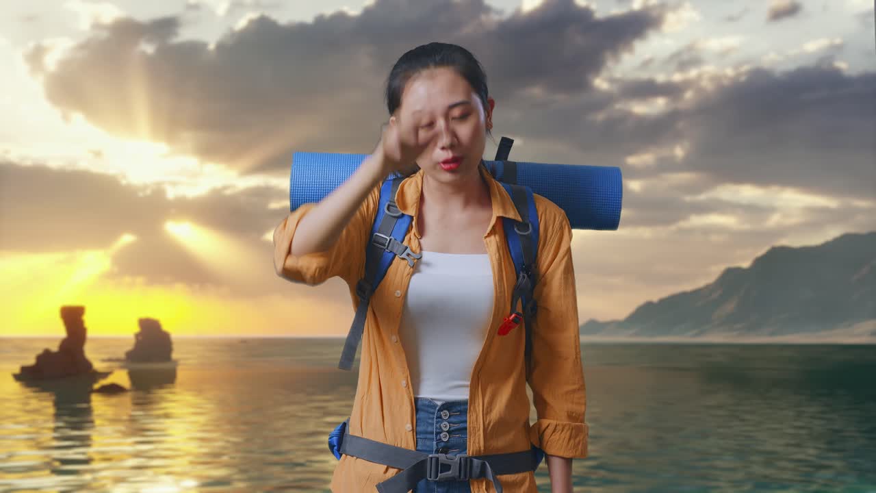 Nữ du khách đi bộ đường dài người châu Á đeo ba lô leo núi tỏ vẻ không hài lòng và hét vào ai đó khi đứng trên bãi biển lúc hoàng hôn