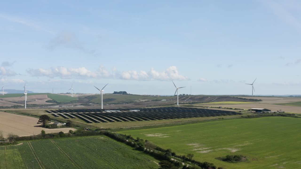 Wind Turbines With Solar Panels In Green Fields Near Saint Newlyn East Countryside In Cornwall, England, United Kingdom