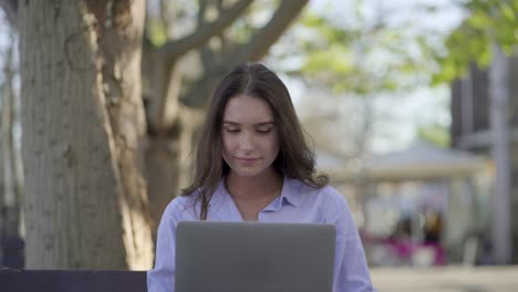 disparo medio de una mujer caucásica bonita en el parque trabajando en una computadora portátil
