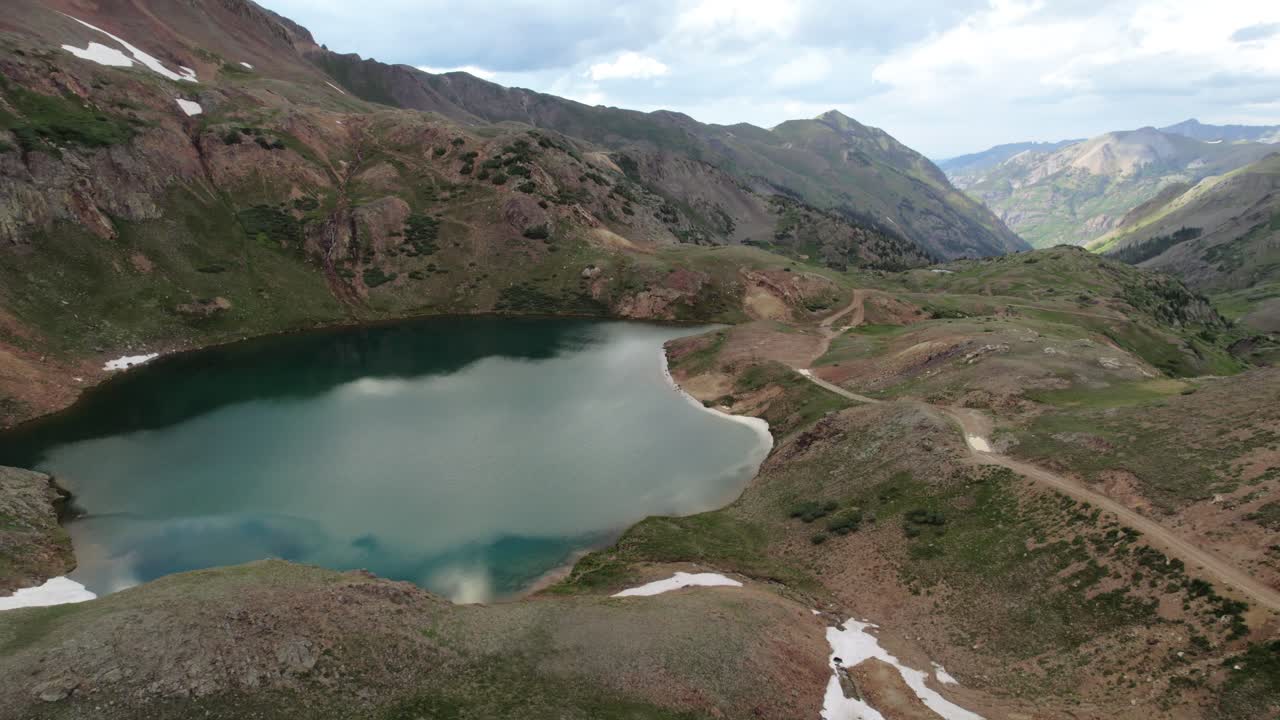 A slow left-moving rotating drone shot of a deep blue glacial alpine lake high in the San Juan Mountains of Colorado in the summertime