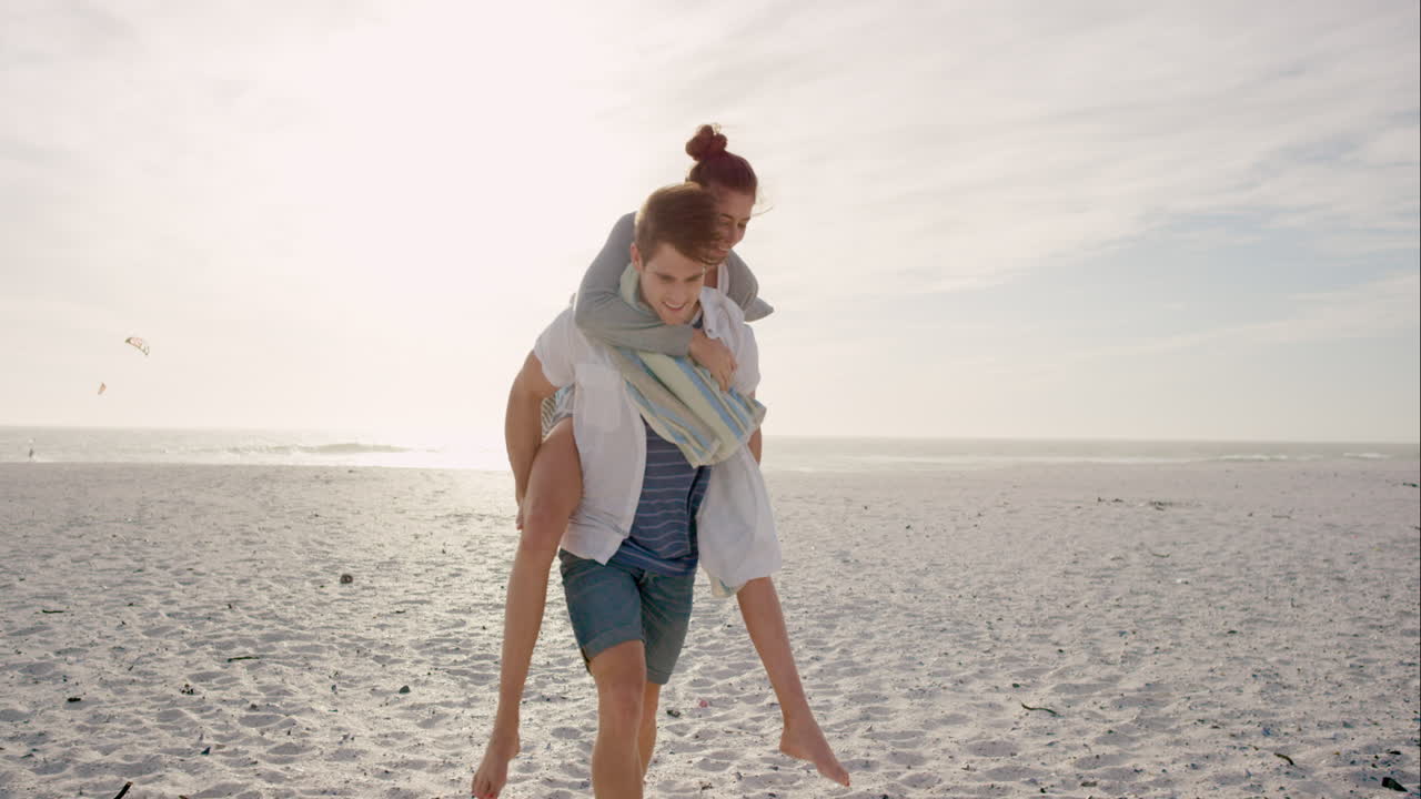 Young couple holding hands walking towards sunset on empty beach