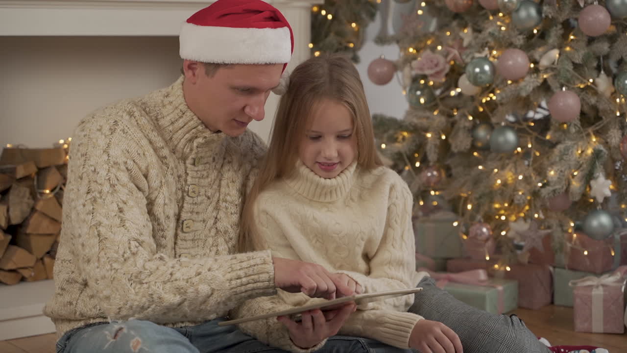 padre e hija usando una tableta en navidad con un sombrero de santa