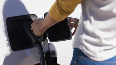 sección media de una mujer caucásica cargando un coche eléctrico