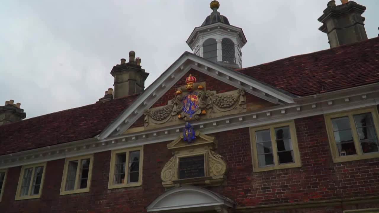Detailed close-up of a traditional English red-brick structure in Salisbury, showcasing ornate royal insignia and a rooftop cupola under a cloudy sky.