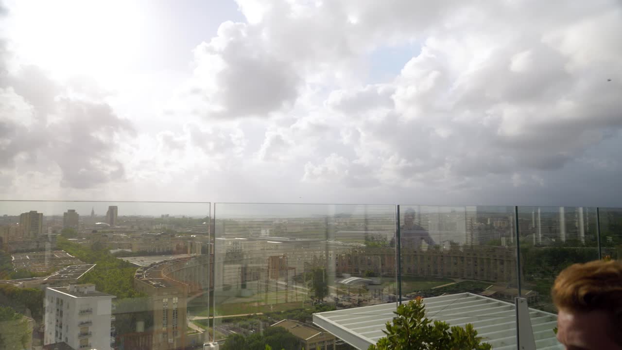 카메라가 도시 풍경을 드러내는 동안 매력적인 백인 남성이 주스를 마시고 있습니다.