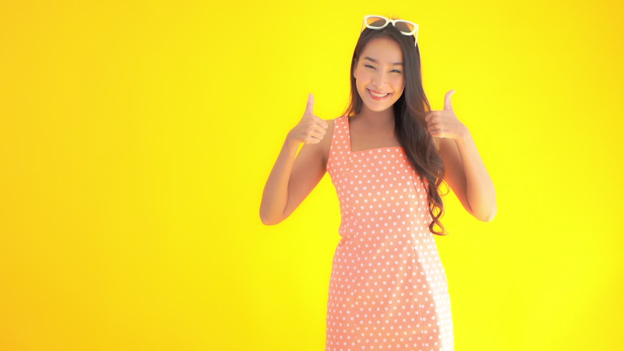 엄지손가락을 치켜드는 노란색 배경에 고립된 매력적인 아시아 여성의 초상화, 정적 샷