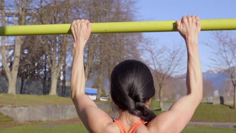 young woman doing pull-ups exercising outdoors