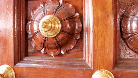 camera slowly zooms in on an intricately carved wooden door with gold accents, highlighting floral motifs and craftsmanship in bright natural light