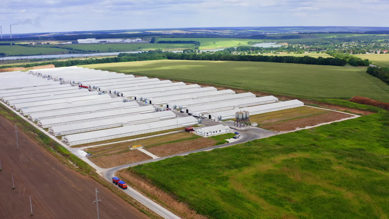 Innovative farm on beautiful landscape. Modern farm buildings on field in summer. White warehouses on green nature. Truck is moving on a road. Aerial view.