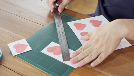 close-up of hands cutting heart shape paper using utility knife cutter with ruler on cutting mat