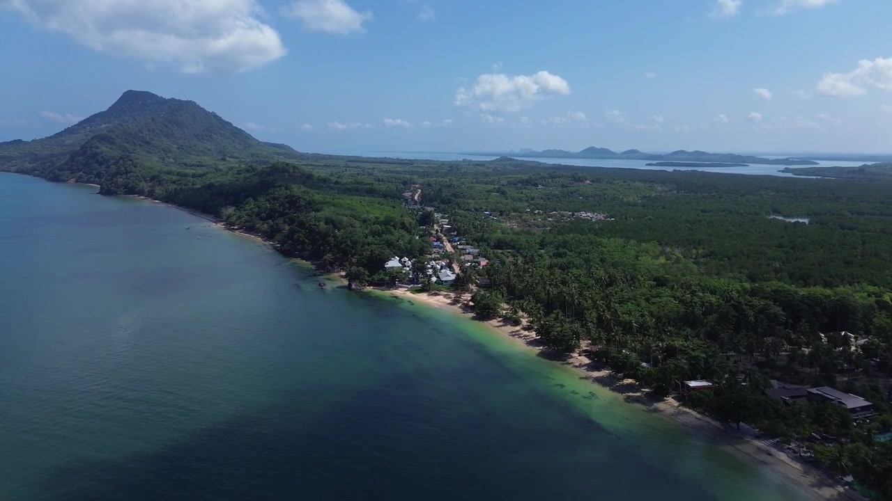 Cinematic aerial footage of Koh Jum Thailand showing lush jungle and a quiet tropical beach in the foreground with island groups and Krabi mainland in background creating a secluded island atmosphere