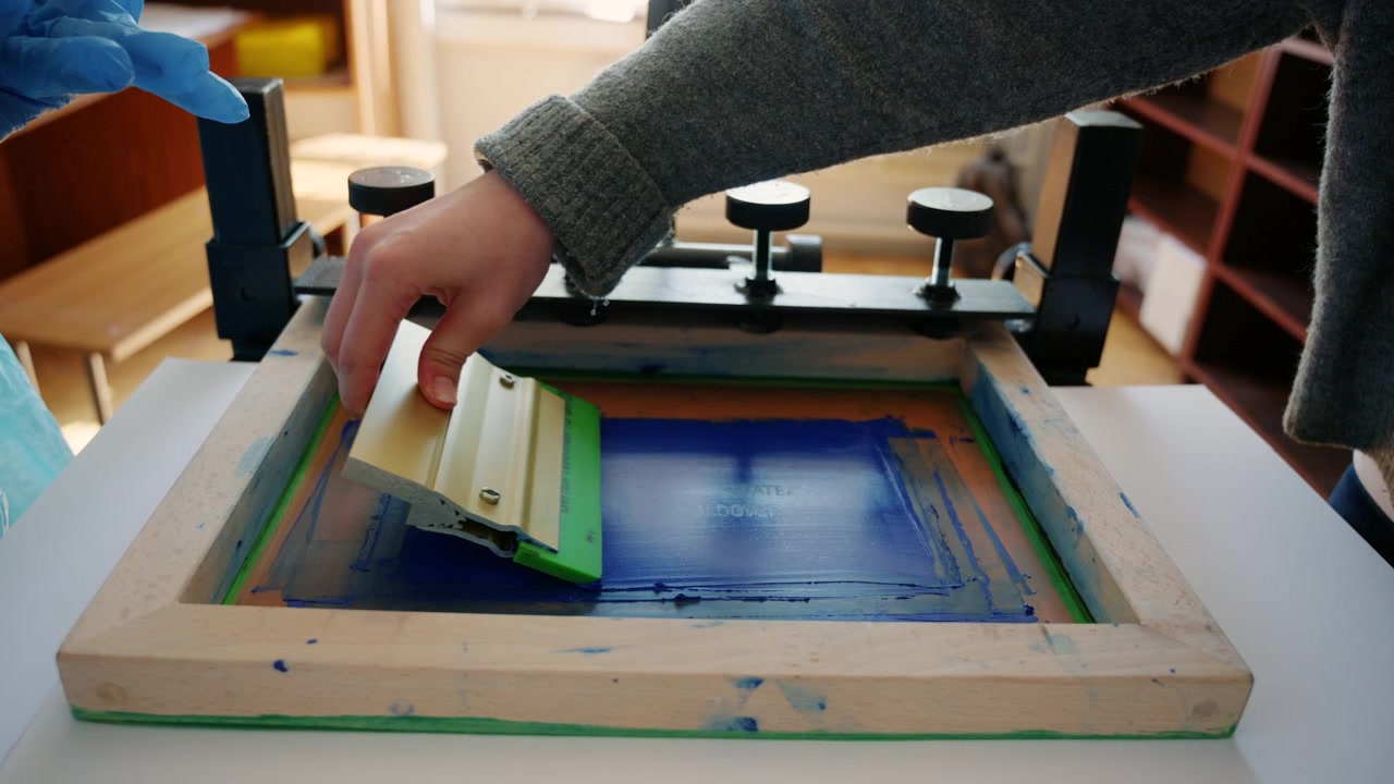 Worker using a squeegee to spread ink across a screen printing frame during textile production
