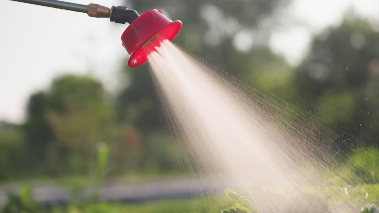 close up red nozzle spraying fine fumigation mist over green plants in backlit field sunlight creating soft glow and droplets agricultural pest control protection scene