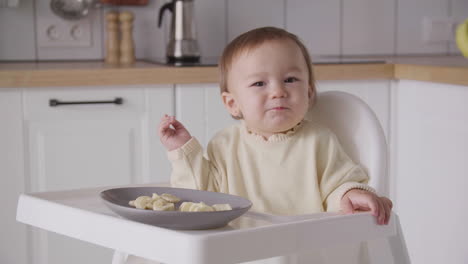 cute baby girl eating banana slices sitting in her high chair in the kitchen 4