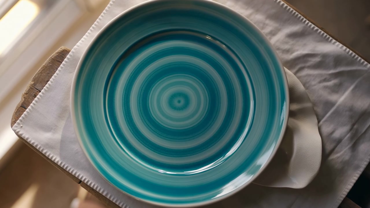 Overhead timepoint showing turquoise concentric ceramic plate on folded white linen near sunlit