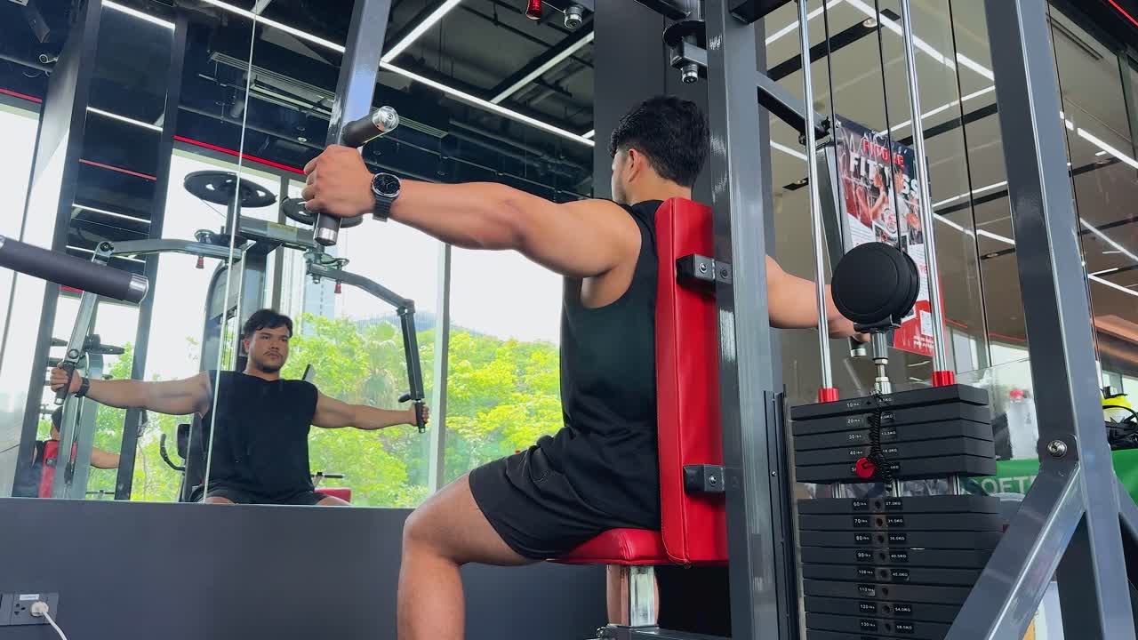 Athletic man in black gym wear does chest fly on pec deck in sunlit gym