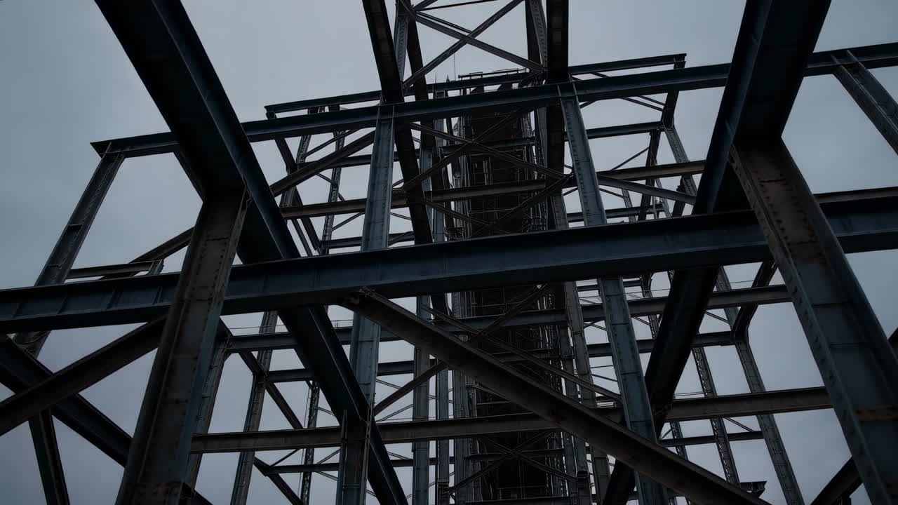 Tilting camera revealing layers of steel framework at base, highlighting height and rusted shaft
