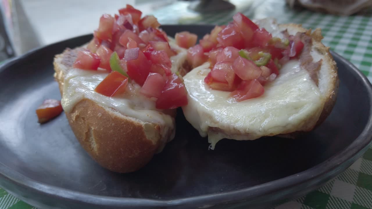 Pull-back close-up showing melted cheese mollete toasts topped with fresh tomato mix