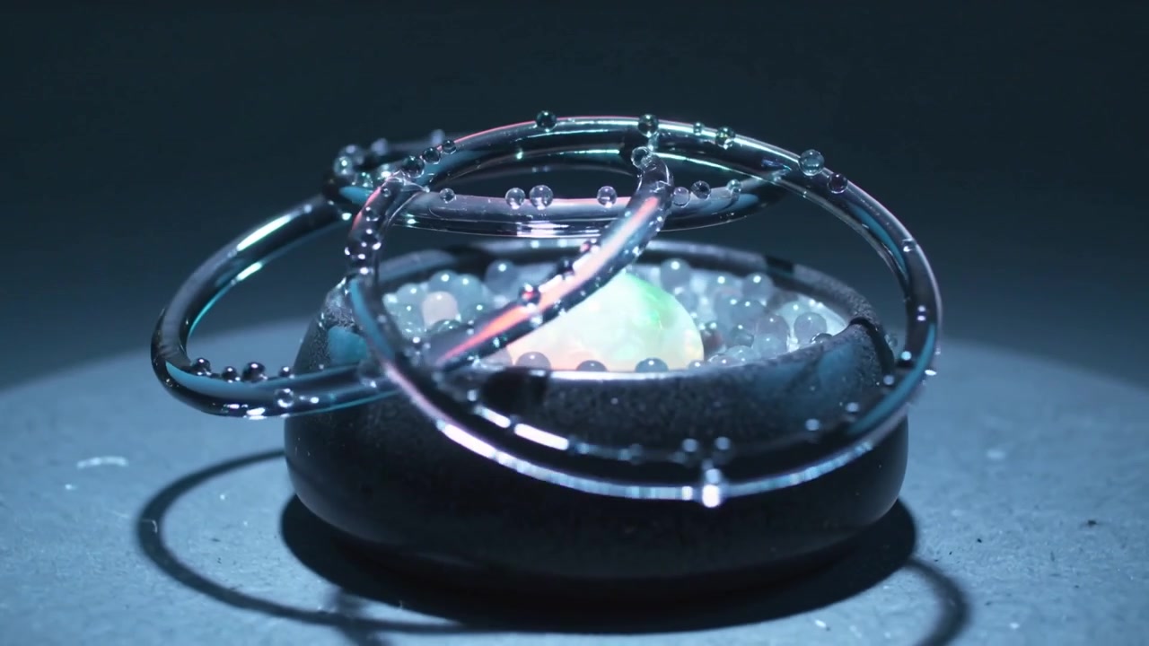Lowering glass rings rotating over bowl on plinth causing orb pulsing, beads and droplets shifting