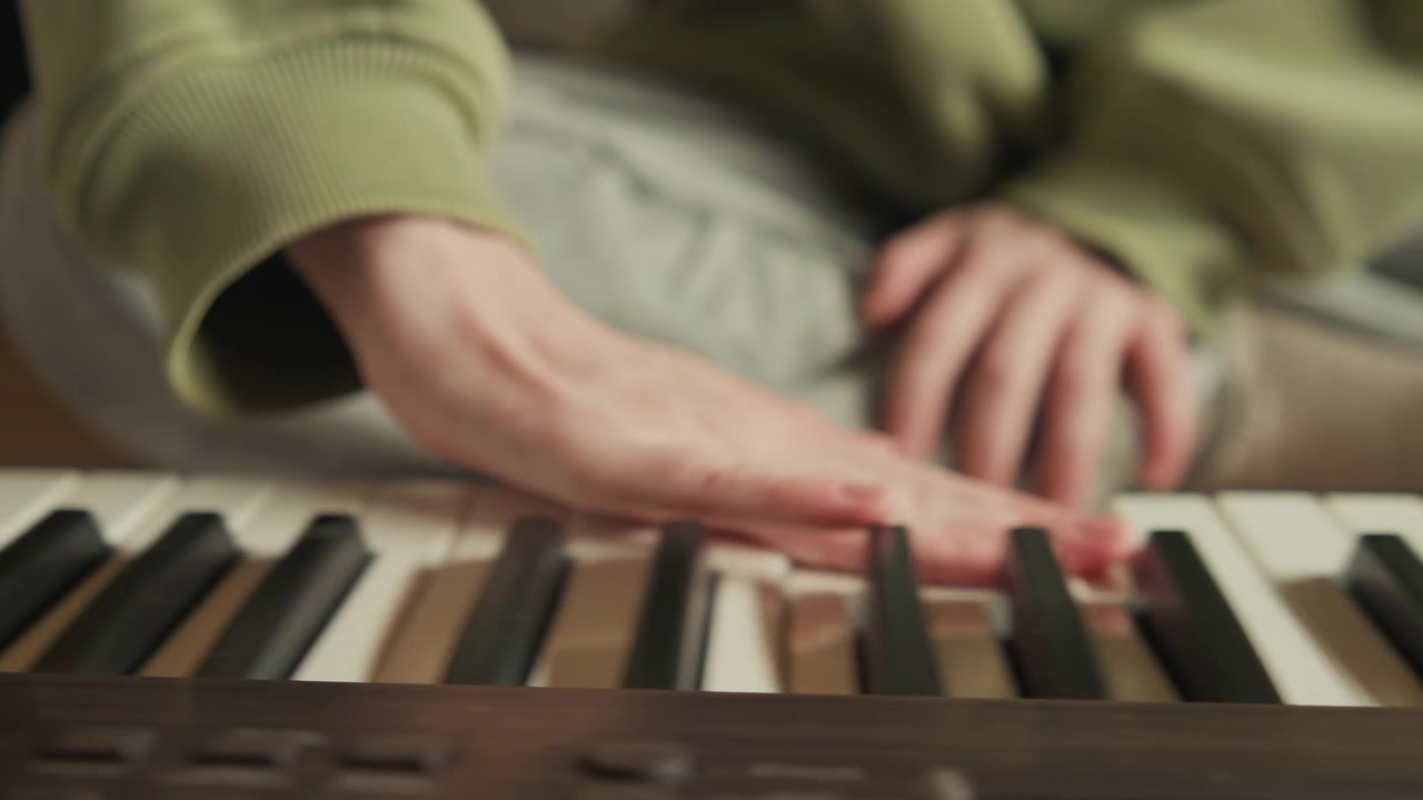 Low angle view of hands actively playing electronic keyboard, fingers pressing black and white keys in warm indoor light, showing rhythmic movement, focused touch, and subtle motion blur