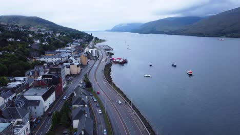 Cars-Driving-Along-Road-Near-Loch-in-Fort-William-Town,-West-Highland-Museum,-Town-Centre---Aerial-Drone-4K-HD-Footage