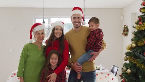 Happy-caucasian-multi-generation-family-wearing-santa-hats-and-looking-at-camera