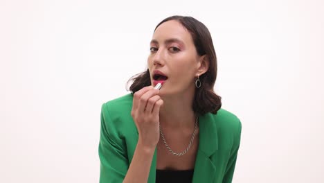 woman applying red lipstick while wearing a green blazer