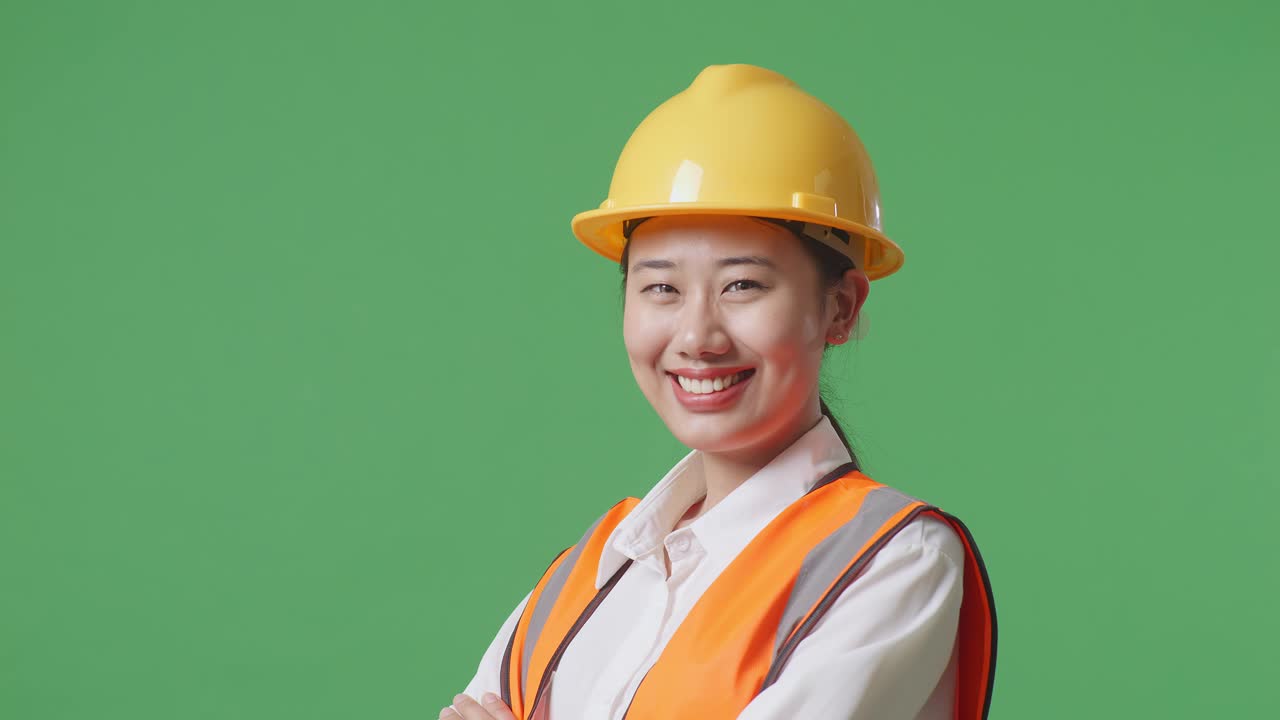 Close Up Side View Of Asian Female Engineer With Safety Helmet Crossing Her Arms And Smiling To Camera While Standing In The Green Screen Background Studio