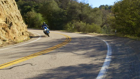 a man in full motorcycle gear riding a motorcycle up a mountain road in the desert hills of california with a blue sky in the background