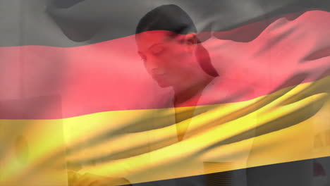 animation of flag of germany over smiling biracial businesswoman using laptop