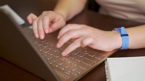 las manos femeninas están escribiendo texto en el teclado de la computadora portátil. los dedos presionan rápidamente las teclas del teclado. hay un cuaderno al lado. computadora personal, trabajo remoto en casa, negocios, estudio, mensajería, chat