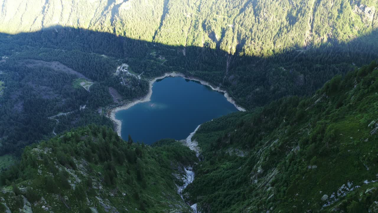 High aerial view looking down steep valley towards Lago di Antrona. Alpine lake surrounded by lush green forest and mountains. For nature or travel content, Piedmont, Italy