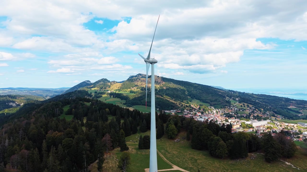 Turbina eolica sopra il villaggio di Sainte-Croix e paesaggio montano svizzero boscoso, ripresa con drone in orbita media di una singola torre.