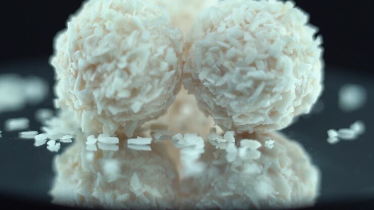 Macro shot of tasty Raffaello bonbons on a rotating reflection stand, coconut dessert, white coco balls, smooth tilt movement 120 fps slow motion video