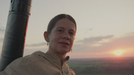 elegant woman gazes confidently toward camera with serene smile while glowing sunset light casts soft highlights on her face, peaceful rural landscape stretching into horizon behind her