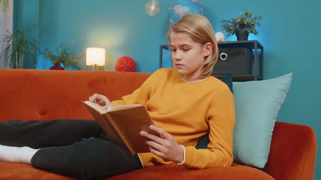 Ein Teenager liest ein Buch, blättert begeistert die Seiten und schaut nachdenklich auf, während er auf dem Sofa liegt