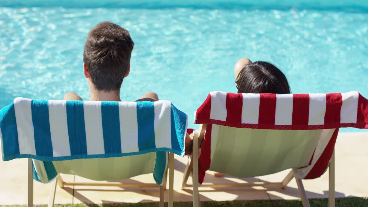 Coppia che si rilassa su sedie a sdraio colorate a bordo piscina.